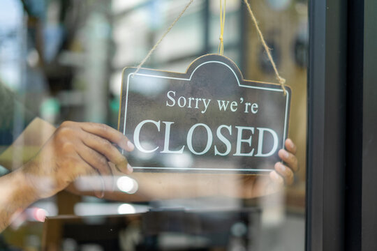 Shopkeeper setting closed sign at coffeeshop. Waiter in medical mask hanging card with closed lettering on cafe entrance door. Small business and startup concept.
