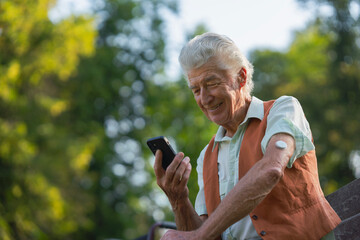 Senior diabetic man checking his glucose data on smartphone outdoors, in park. Elderly man with...
