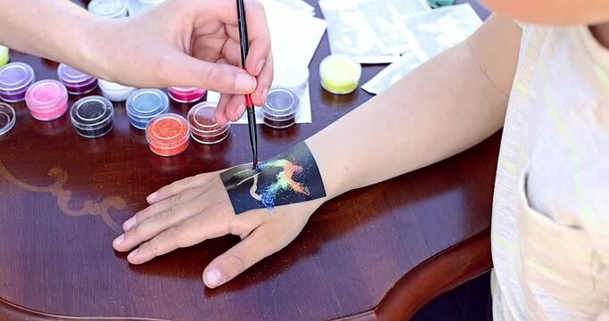Kid's animator is creating a Shimmering sparkling glitter tattoo on a child's hand at a birthday party