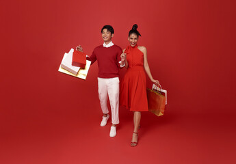 Happy asian couple in red casual attire holding shopping bag and walking shopping in chinese new...
