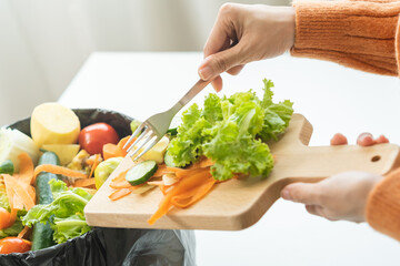 Compost from leftover food, asian young housekeeper woman hand holding cutting board use fork scraping waste, rotten vegetable throwing away into garbage, trash or bin. Environmentally responsible.
