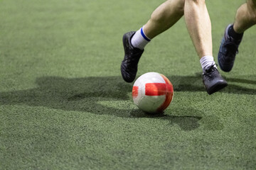 Futsal player hitting the ball on artificial football field indoors.