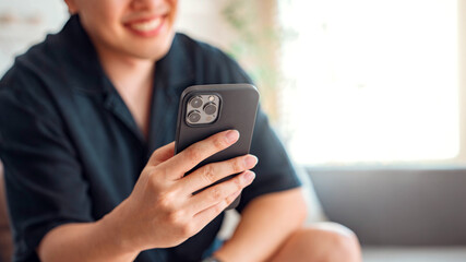 Closeup hand of relaxed man using smartphone while sitting on couch in living room at home, Browsing internet or messaging with friends.