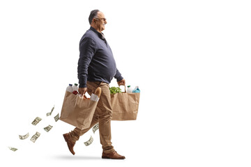 Full length profile shot of a mature man carrying grocery bags and money falling behind