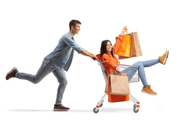 Young man pushing a female with shopping bags inside a shopping cart