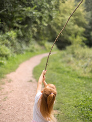 rothaariges Kind spielt mit einem Stock auf einem ruhigen Waldweg – natürliche Außenszene...