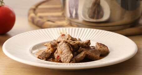 Serving the dish. Cooked meat from the pan is placed on a plate. Beef Goulash. Food on the table. Close-up shot.
