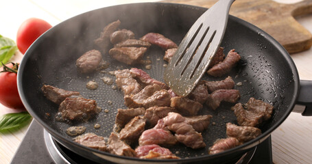 Sliced pieces of raw meat are mixed with a spatula in a frying pan. Roasting beef in a pan. Cooking in the kitchen. Food preparation.