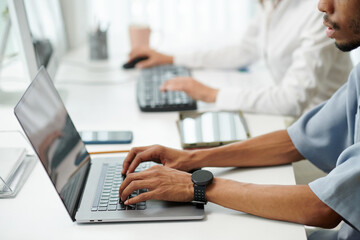 Hands of software developer with smartwatch working on laptop in office