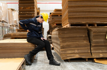 Warehouse worker sitting on the floor in front of stack of cardboard boxes with pain in the back due to frequently lifting heavy objects