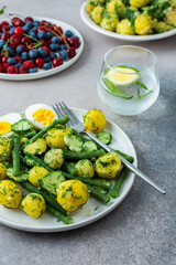Delicious lunch or dinner, boiled young potatoes with asparagus beans and young fresh cucumbers, boiled eggs and fresh berries, refreshing water with lemon and mint