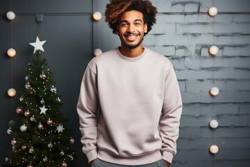 Portrait happy guy posing wearing plain apricot hoodie against Christmas tree and festive lights garland background. Copy space. Xmas holiday.