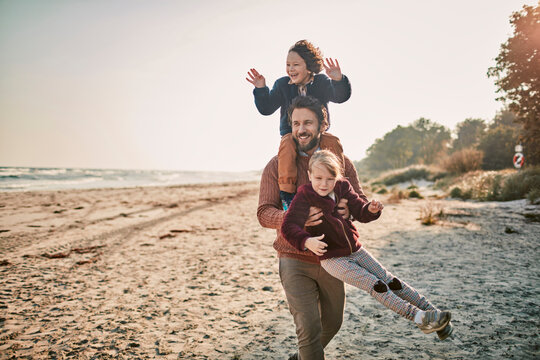 Happy young father taking his kids for a walk on a sandy beach during winter