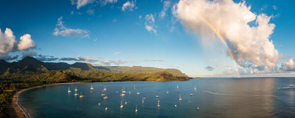 Aerial view of rainbow and sunlit clouds over the mountain peaks of Na Pali coast across Hanalei...