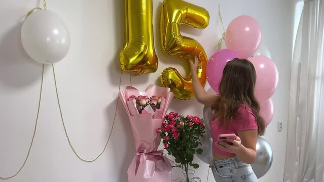 teen girl celebrates birthday 15th anniversary balloons flowers numbers on white wall take pictures shoot on video for social networks on Internet holiday decorate room decorations. jeans