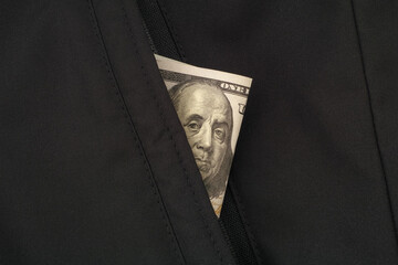 A one hundred dollar bill in the pocket of a black jacket