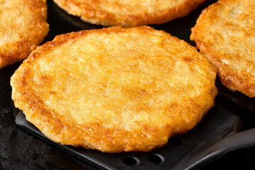 Detail of potato pancakes on cast iron frying pan with black spatula.