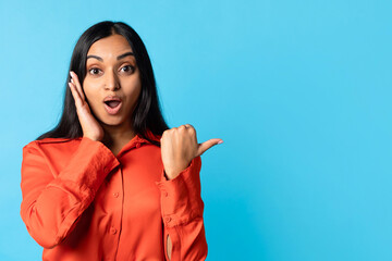Shocked Indian Young Woman Pointing Thumbs Finger Aside, Blue Background
