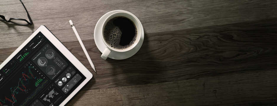 top view Cup of coffee with digital tablet computer, business finance charts and pen on wood background.