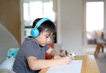 Happy kid wearing some headphones and listening to music while drawing on paper, Indoor portrait by...