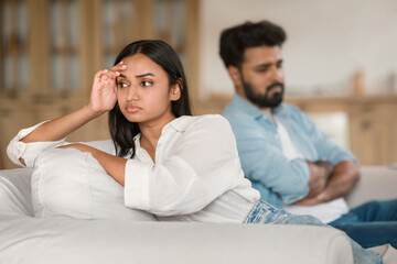 Unhappy indian couple having quarrel, depressed man and woman sitting on couch, experiencing difficulties in marriage