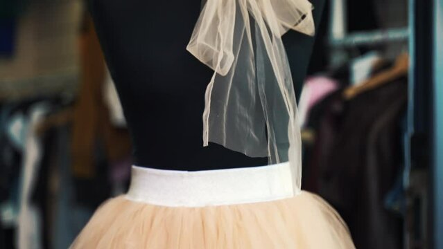 Fashionable tulle skirt and tired bow on tailor mannequin in tailor workshop, peach colour handmade clothing on store window, professional atelier manufacturing fashion designer's garment, dressmaker