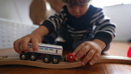 Child playing with toys at home, close-up little boy hand plays with traditional vintage retro railroad wagons on wooden tracks