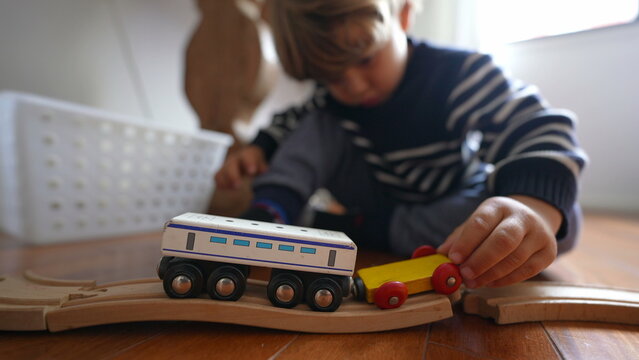 Child playing with toys at home, close-up little boy hand plays with traditional vintage retro railroad wagons on wooden tracks