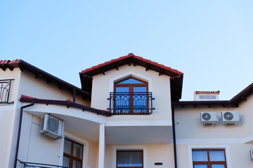 Stucco house with orange tile roof, chimney and rain gutter with downspout, balcony, outdoor air conditioner units against blue sky. High quality photo