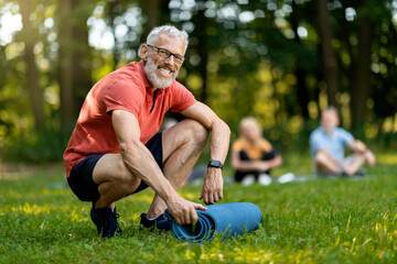 Handsome Senior Man Rolling Yoga Mat After Group Lesson Outdoors