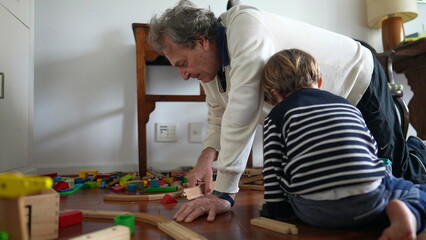 Fototapeta premium Grandfather and Grandson Constructing Train Tracks on Hardwood Floor, Elderly Man and Young Boy Building Train Set on Wooden Floor