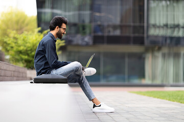 Side view of middle eastern young man using laptop outdoors