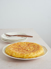 whole homemade Spanish potato omelette on a plate on the table ready to eat; next to it cutlery, fork and knife on serving plates.