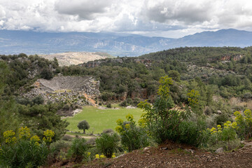 Fototapeta na wymiar An antique panoramic landscape. A wide juicy green pasture with sheep. Ancient white stone ruins, damaged amphitheater and many small rocks are around. 