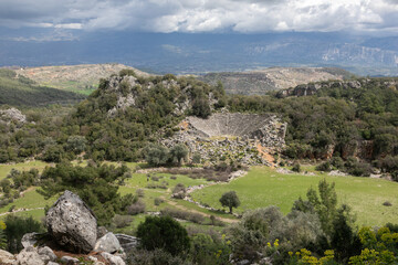 Fototapeta na wymiar An antique panoramic landscape. A wide juicy green pasture with sheep. Ancient white stone ruins, damaged amphitheater and many small rocks are around. 