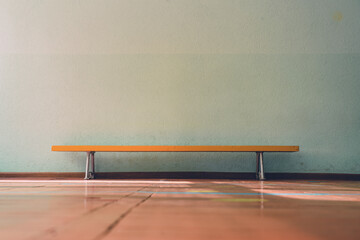 Yellow wooden old bench standing on floor indoor of medical rehabilitation center inside with empty concrete wall with copy space - obrazy, fototapety, plakaty