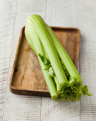 Fresh celery on a wooden board on a white wooden background. Healthy eating.