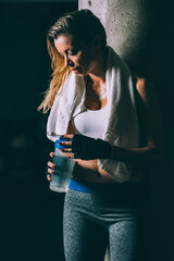 Fit blonde tired woman resting and drinking after training working out in Gym