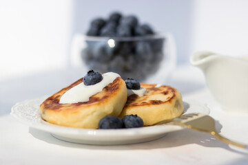 Cheese pancakes with blueberries on a white table. Morning rays of the sun. Good morning postcard