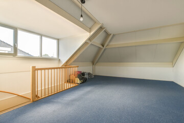 Interior of attic room with blue carpeted floor and wooden railing
