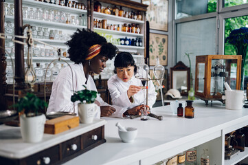 Two multicultural pharmacists are using glass funnels for cure making.