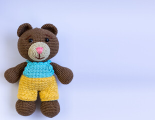 Knitted bear on a white background in a yellow and blue suit. Space for text