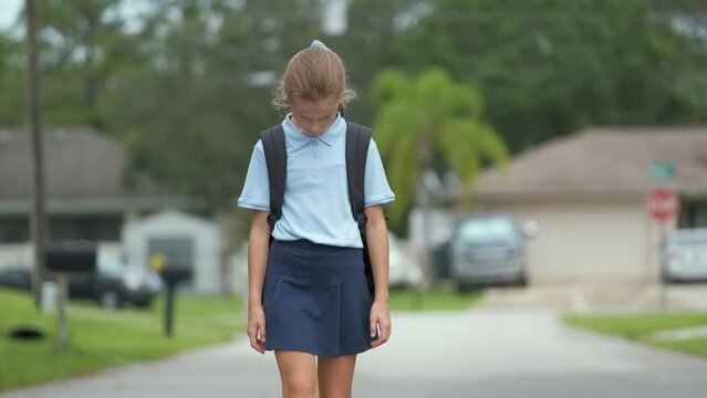Depressed young student girl walking on suburban street returning home from school. Concept of broken friendship