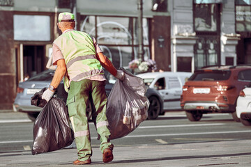 A male janitor removes garbage bags from the streets of the city. The city service takes care of...