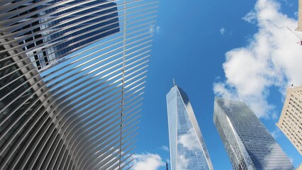 Timelapse, amazing view of the the Freedom Tower, One World Trade Center and Oculus in Lower Manhattan, New York against the cloudy blue sky reflecting on the glass skyscraper