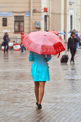 A fashionable young girl walks around the city under a red umbrella. Rainy weather on an autumn day outside.