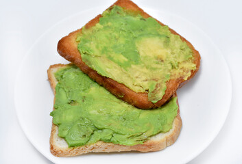 Avocado pasta on fried toast. Vegetables spread on bread. Vegan breakfast on a white plate.