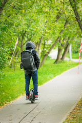 Young man with backpack on motorized unicycle riding trough the city park in summer day