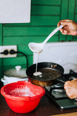 A woman cook pours batter for pancakes with a ladle into a frying pan. Food photography.