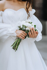 The bride in a white lace dress holds a bouquet of flowers from peonies, roses close-up. Wedding photography, portrait.